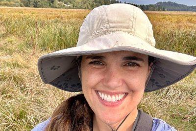 woman with wide brim hat stands in a grassy plain